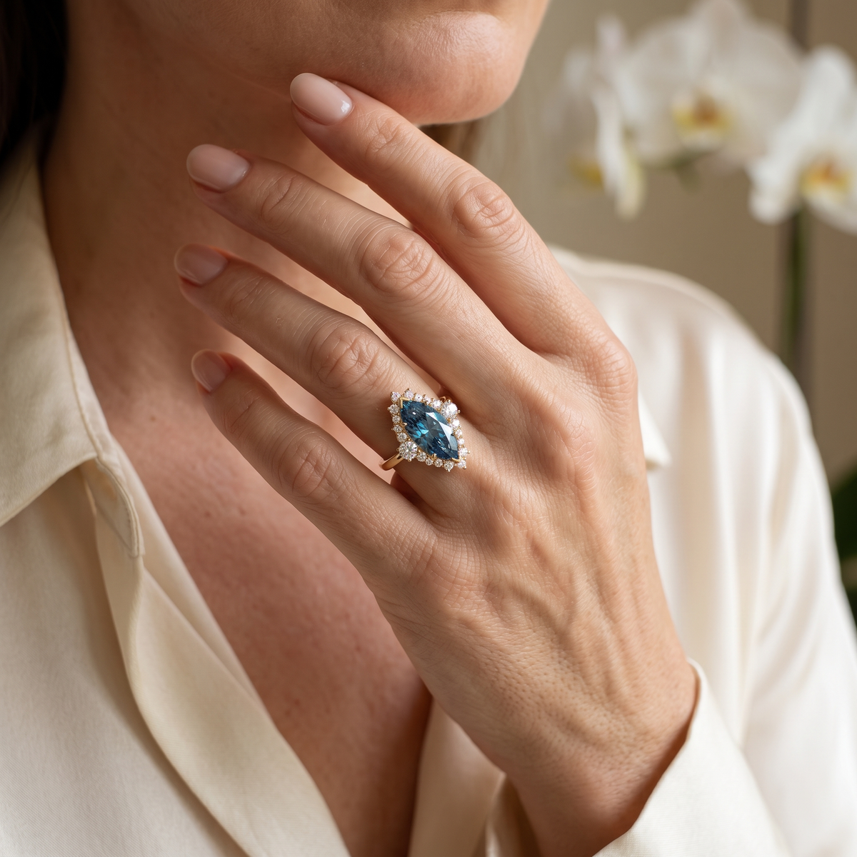 Close-up lifestyle view of a marquise-cut blue moissanite halo ring in rose gold worn on a hand.