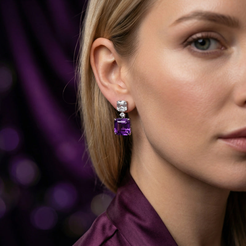 Woman wearing a square cut natural amethyst and silver drop earring against a dark purple background.