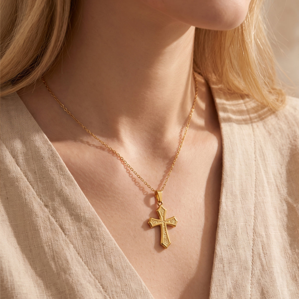 Model wearing the gold-tone filigree cross necklace with a beige V-neck top.