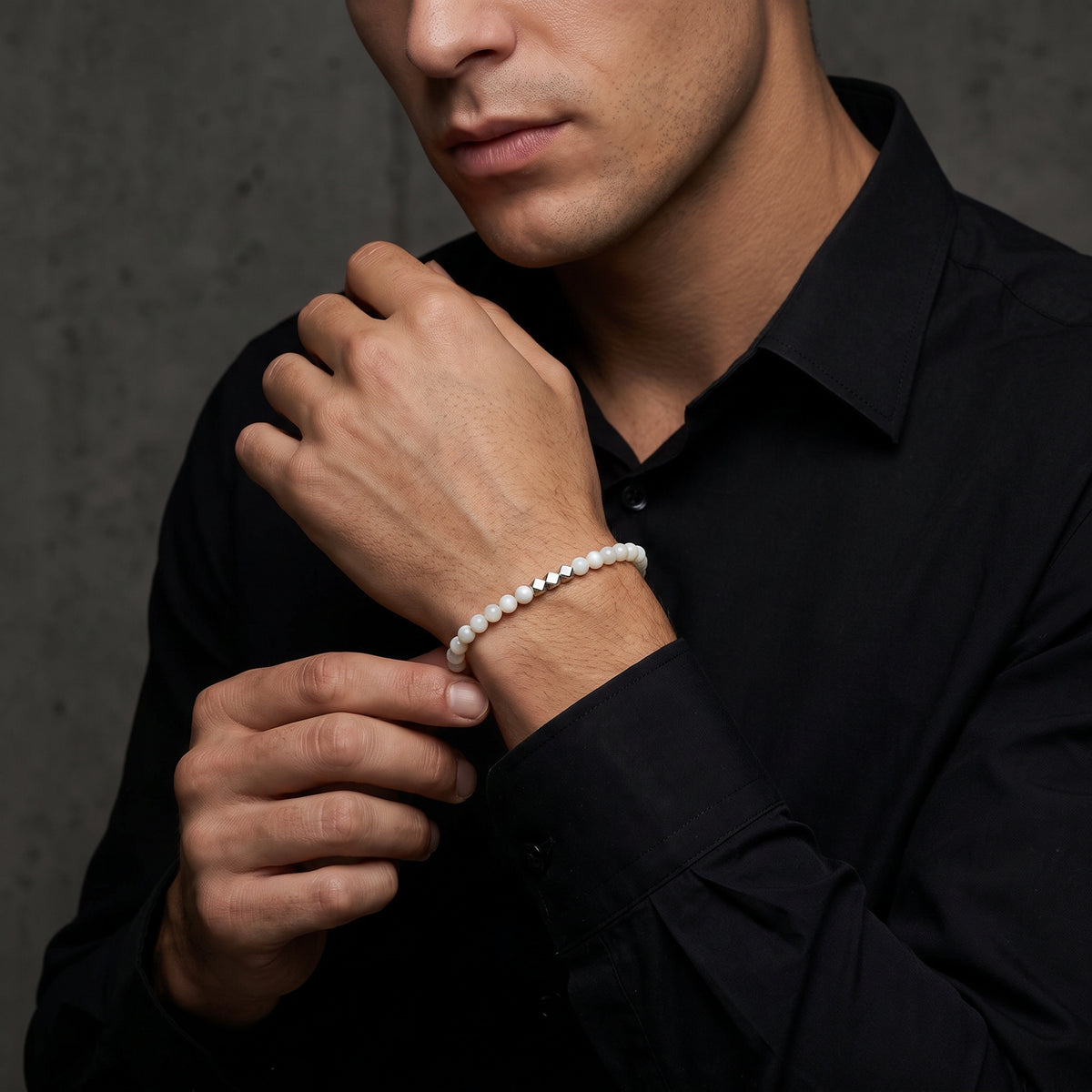 Close-up of a man wearing the white beaded bracelet with silver cube accents over a black collared shirt.