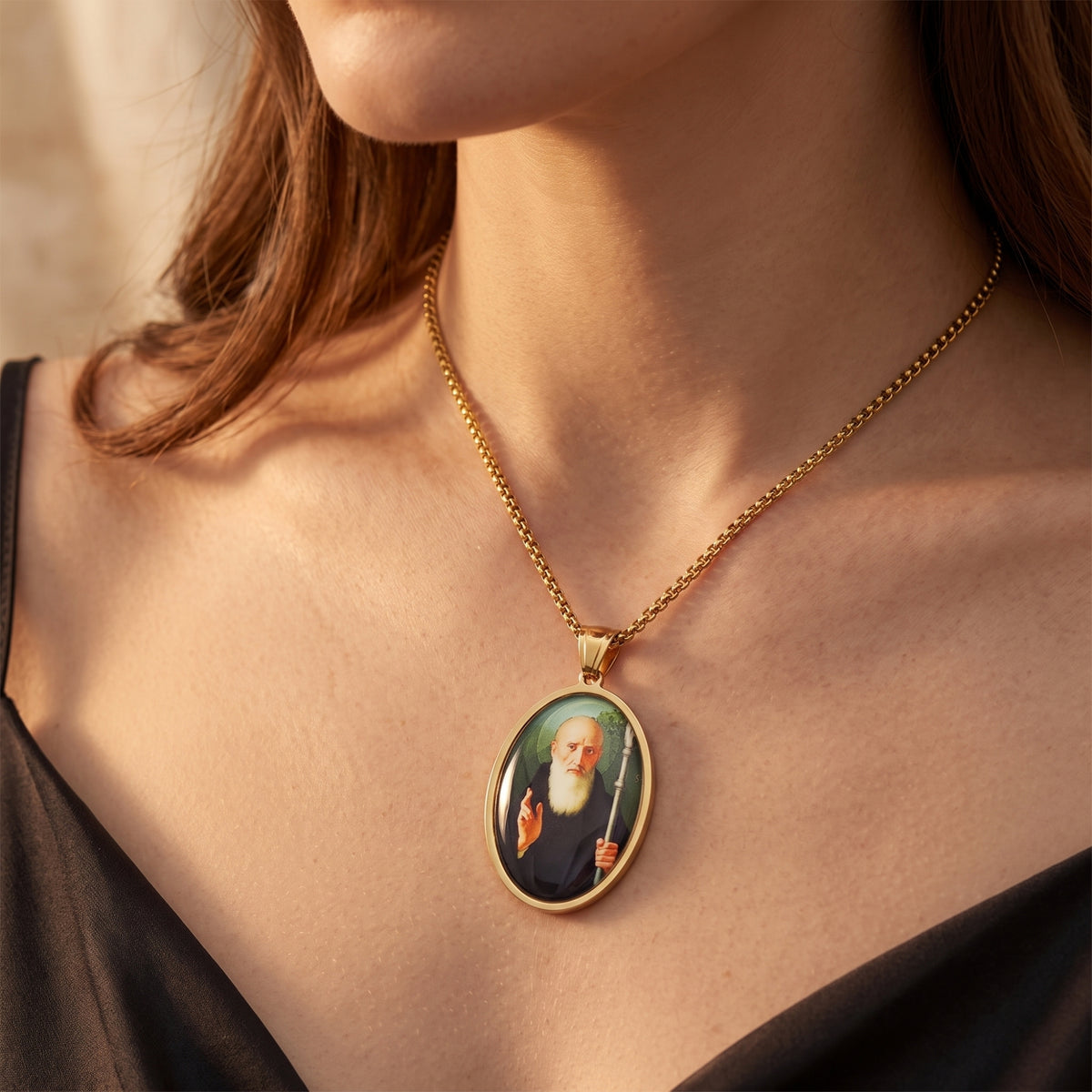 Gold-tone saint medallion necklace worn on a woman's neck above a black top.