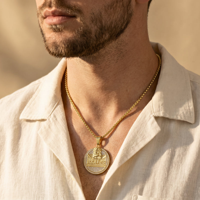 Close-up of a man wearing the gold-tone Last Supper medallion necklace with an open cream shirt.