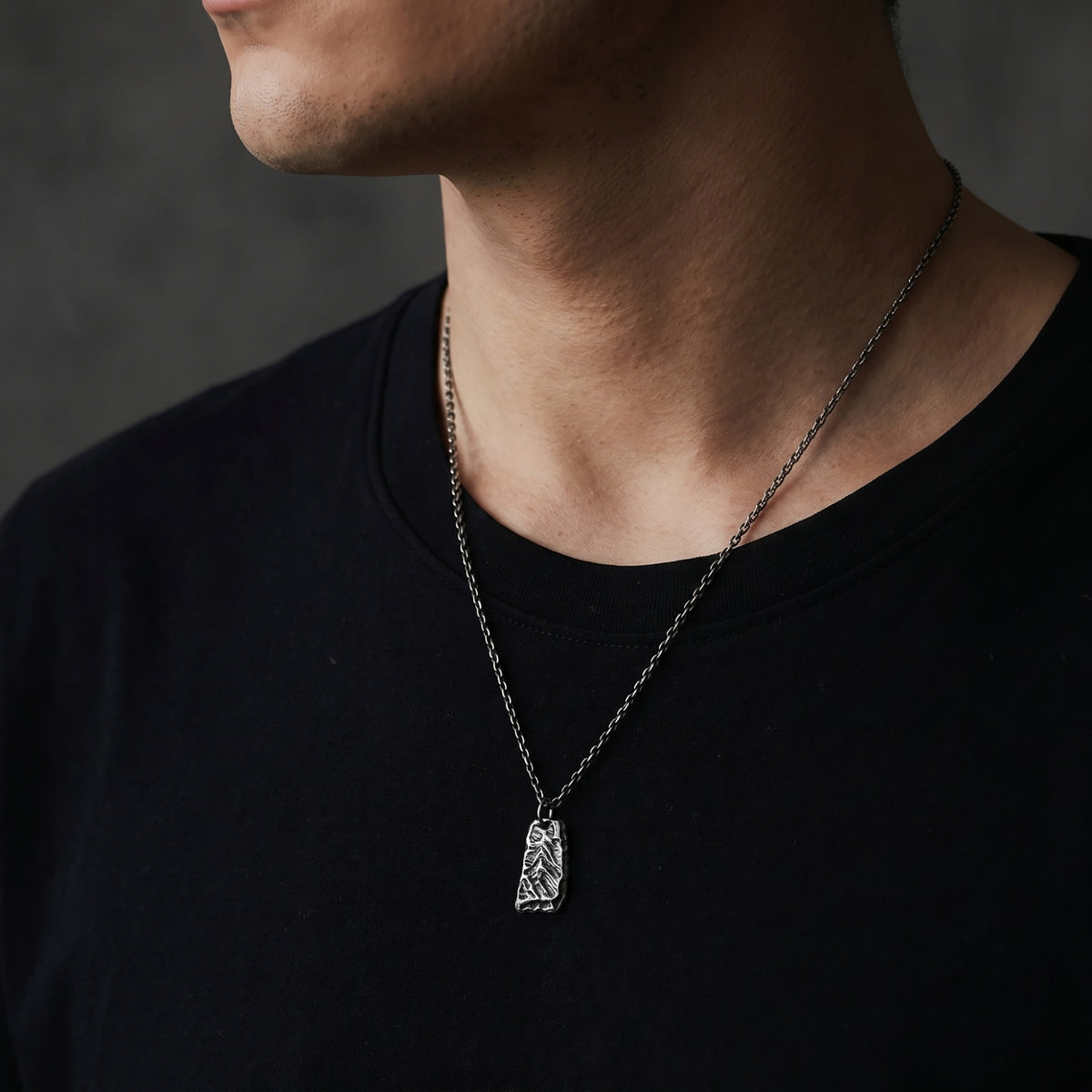 Side-angle view of a man wearing the textured silver pendant necklace over a black T-shirt.