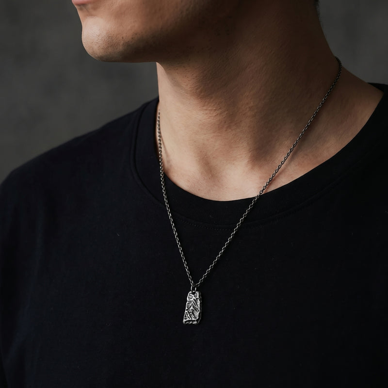 Side-angle view of a man wearing the textured silver pendant necklace over a black T-shirt.