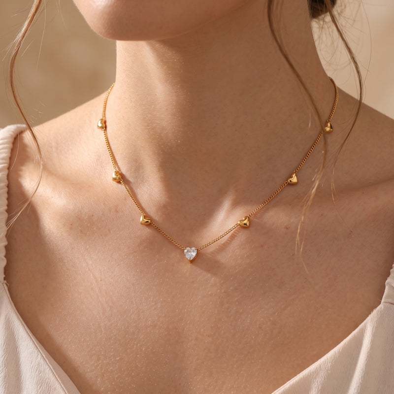 Model wearing the 18K gold Amoris heart necklace featuring a central heart-cut simulated diamond pendant.