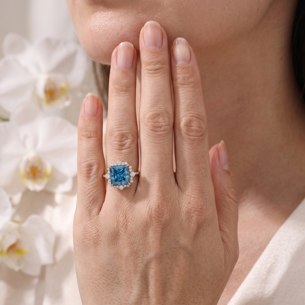 Model wearing a rose gold princess-cut blue moissanite halo ring on her hand.