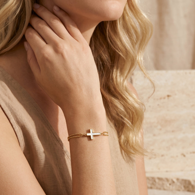 Model wearing the gold double-strand bead bracelet with a mother-of-pearl cross charm on her wrist.