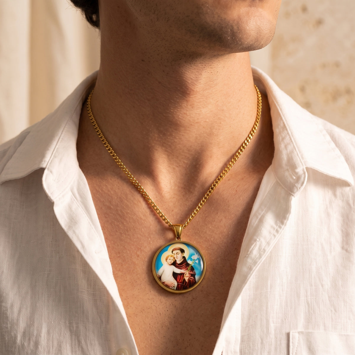Man wearing a gold-tone Saint Anthony medallion necklace with an open-collar white shirt.