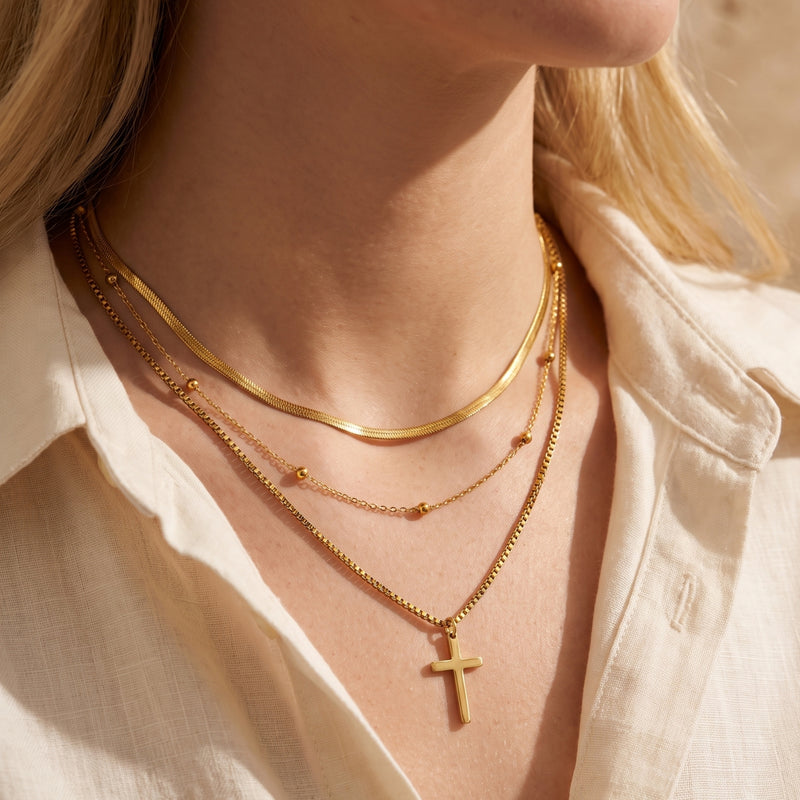Close-up of a model wearing a gold-tone triple-layered cross necklace with an open cream shirt.