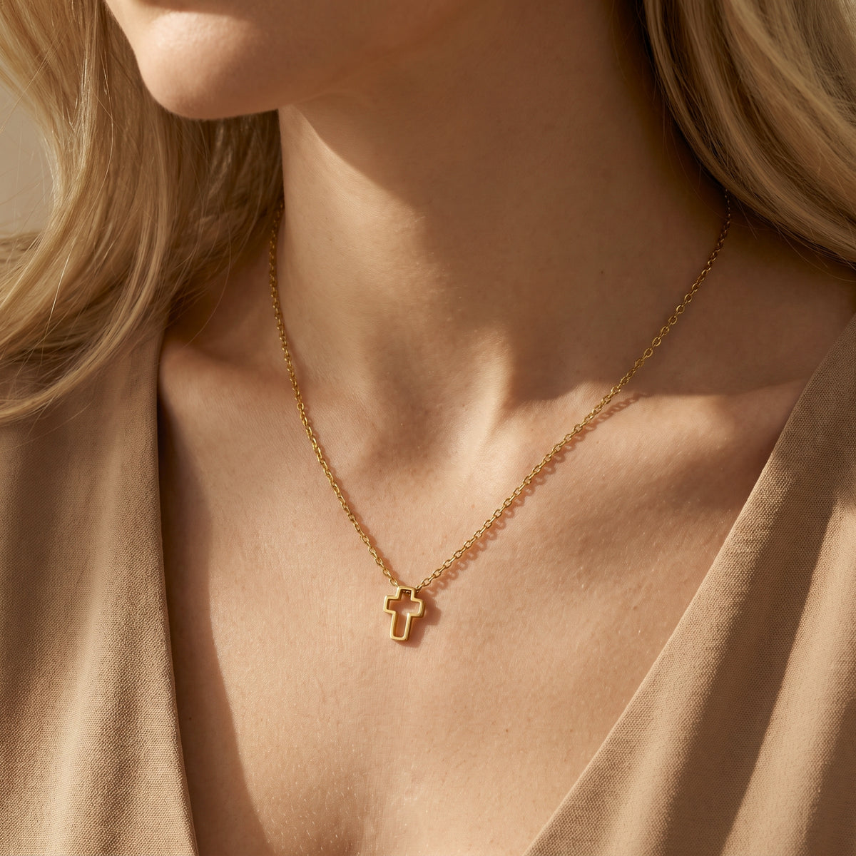 Close-up of a model wearing a gold-tone openwork cross necklace with tan fabric framing the neckline.