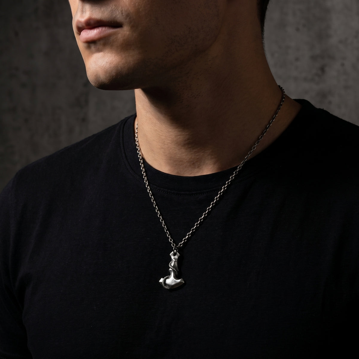 Close-up view of a man wearing the silver Mjolnir hammer pendant necklace against a black T-shirt.