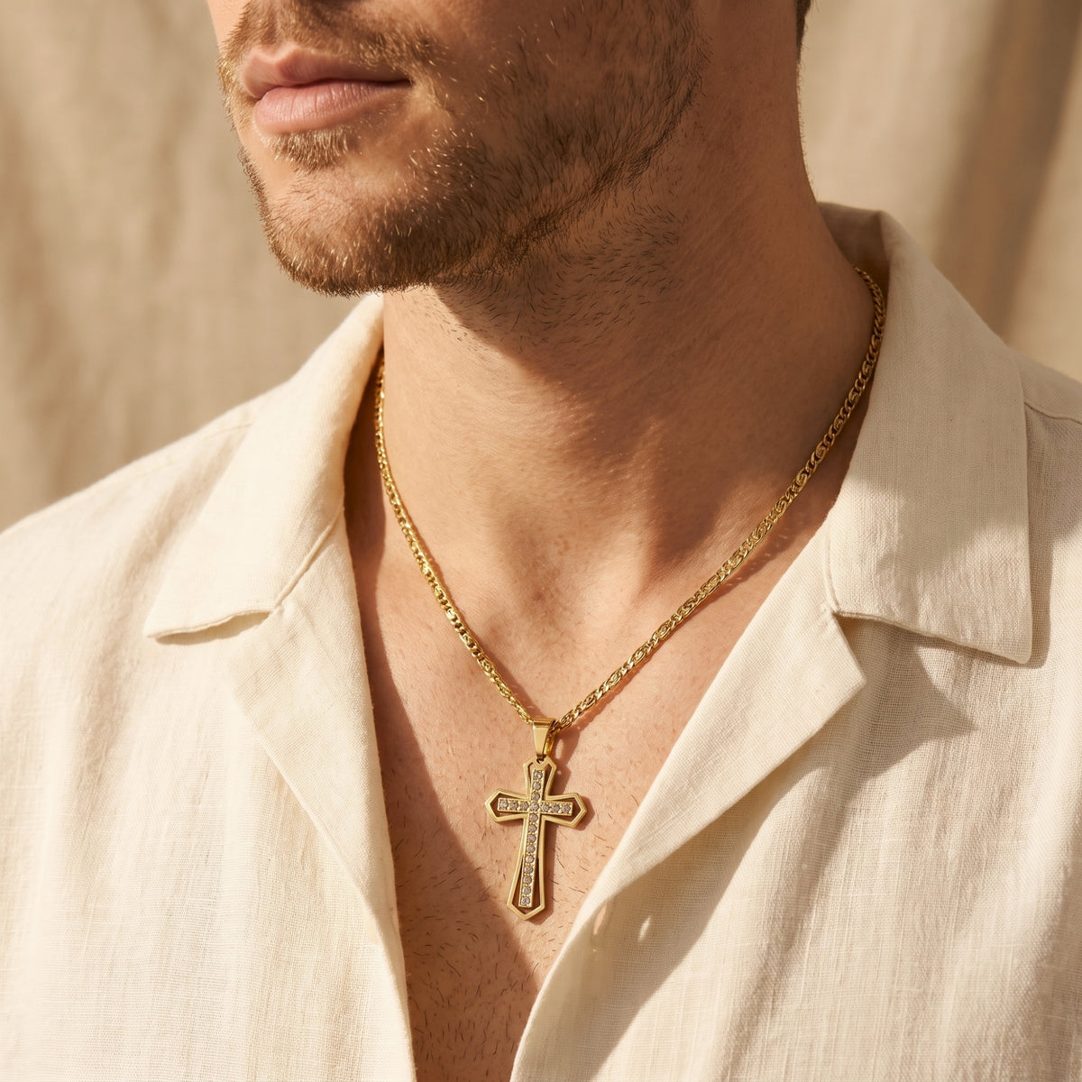 Side perspective of a man wearing the gold-finish crystal cross necklace with an open cream linen shirt.