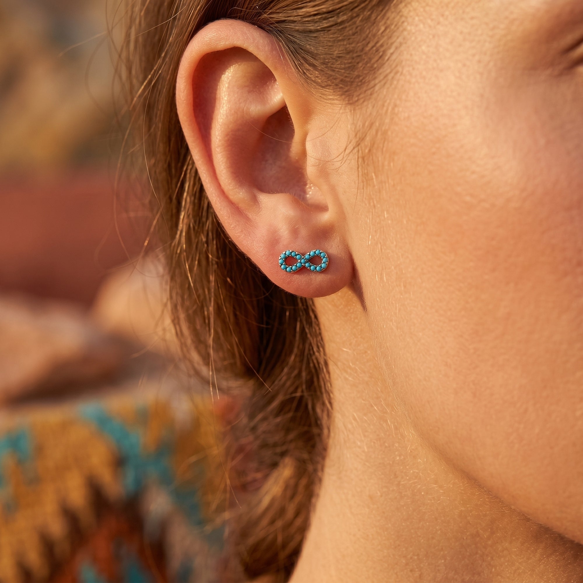 Woman wearing a silver infinity stud earring with turquoise stones in a Southwestern-inspired setting.