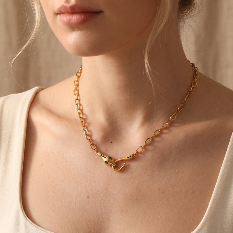 Gold finish stainless steel Serpentine Necklace with a sculptural snake head clasp worn on a woman's neck.
