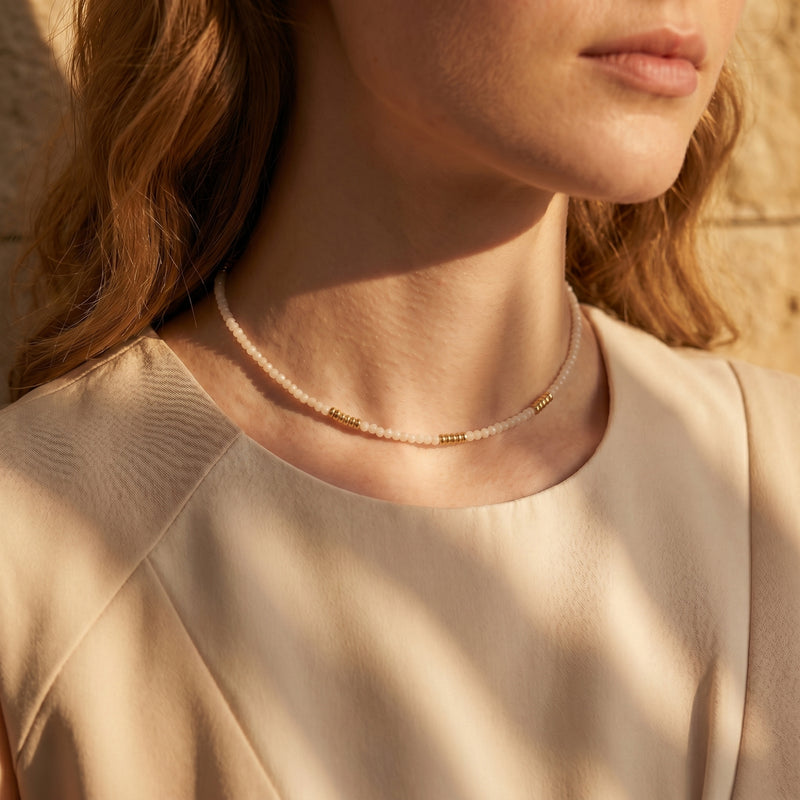 Gold-tone and white quartz beaded necklace worn on a woman's neck in soft natural light.