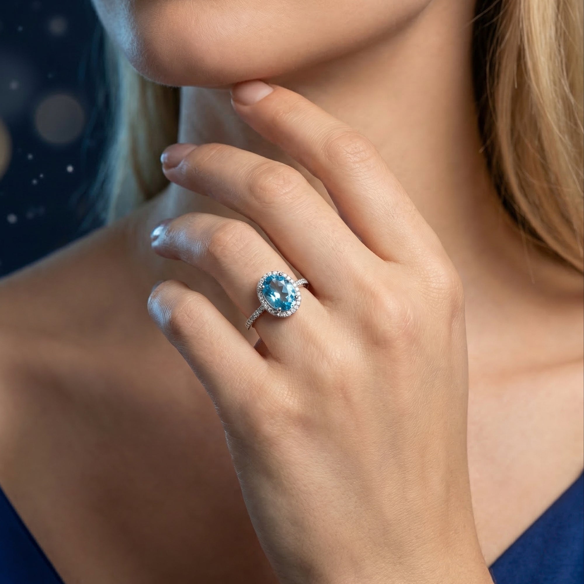 The Ariella oval cut blue topaz halo ring in sterling silver worn on a woman's hand.
