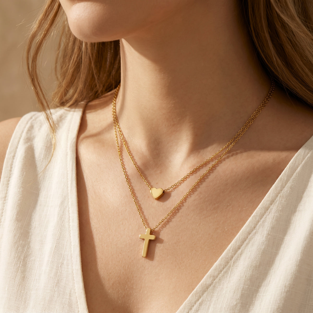 Close-up frontal view of a woman wearing the layered gold-tone necklace with heart and cross pendants.
