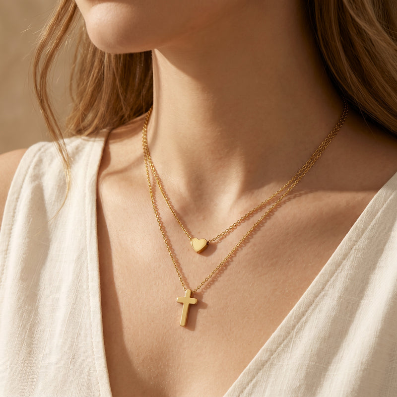 Close-up frontal view of a woman wearing the layered gold-tone necklace with heart and cross pendants.