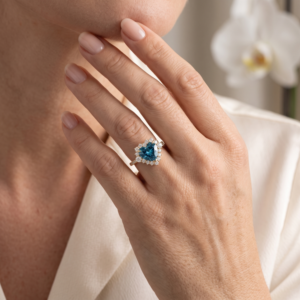 Close-up of a model wearing a rose gold heart-cut teal blue moissanite halo ring.