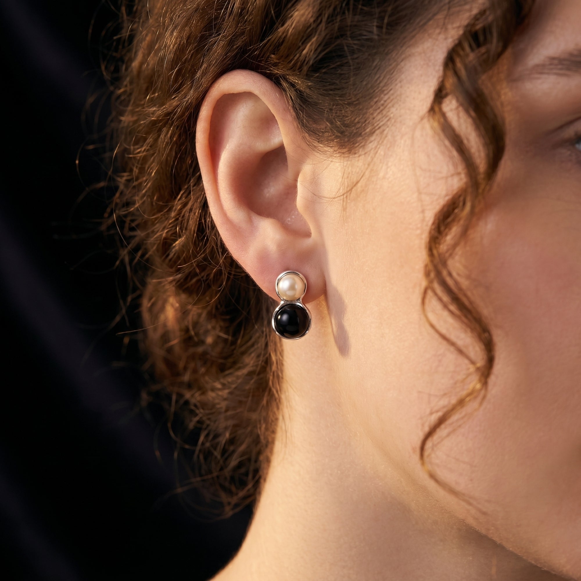 Woman wearing a silver drop earring featuring a round white pearl and black onyx cabochon.