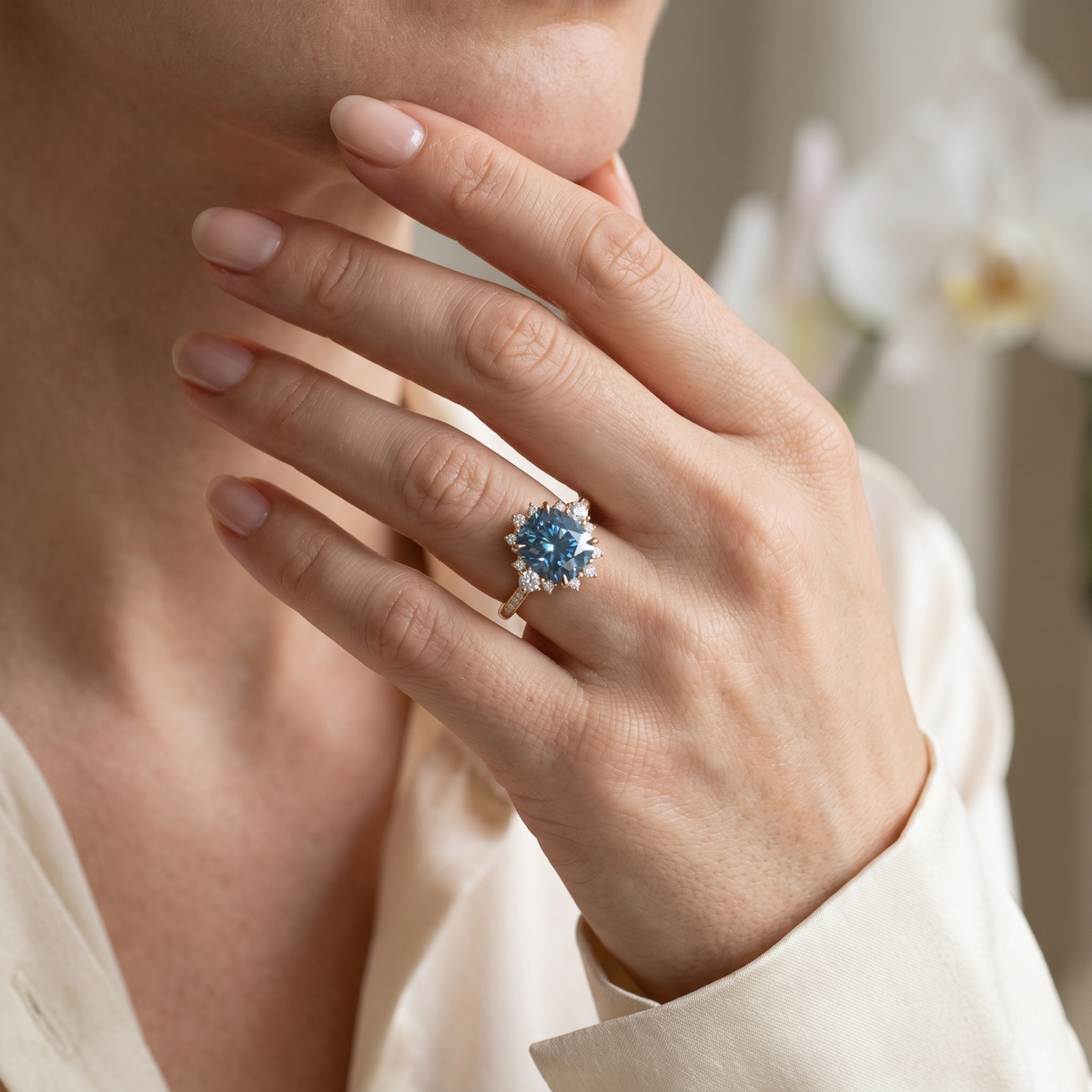 Close-up of a model wearing a yellow gold blue moissanite halo engagement ring.