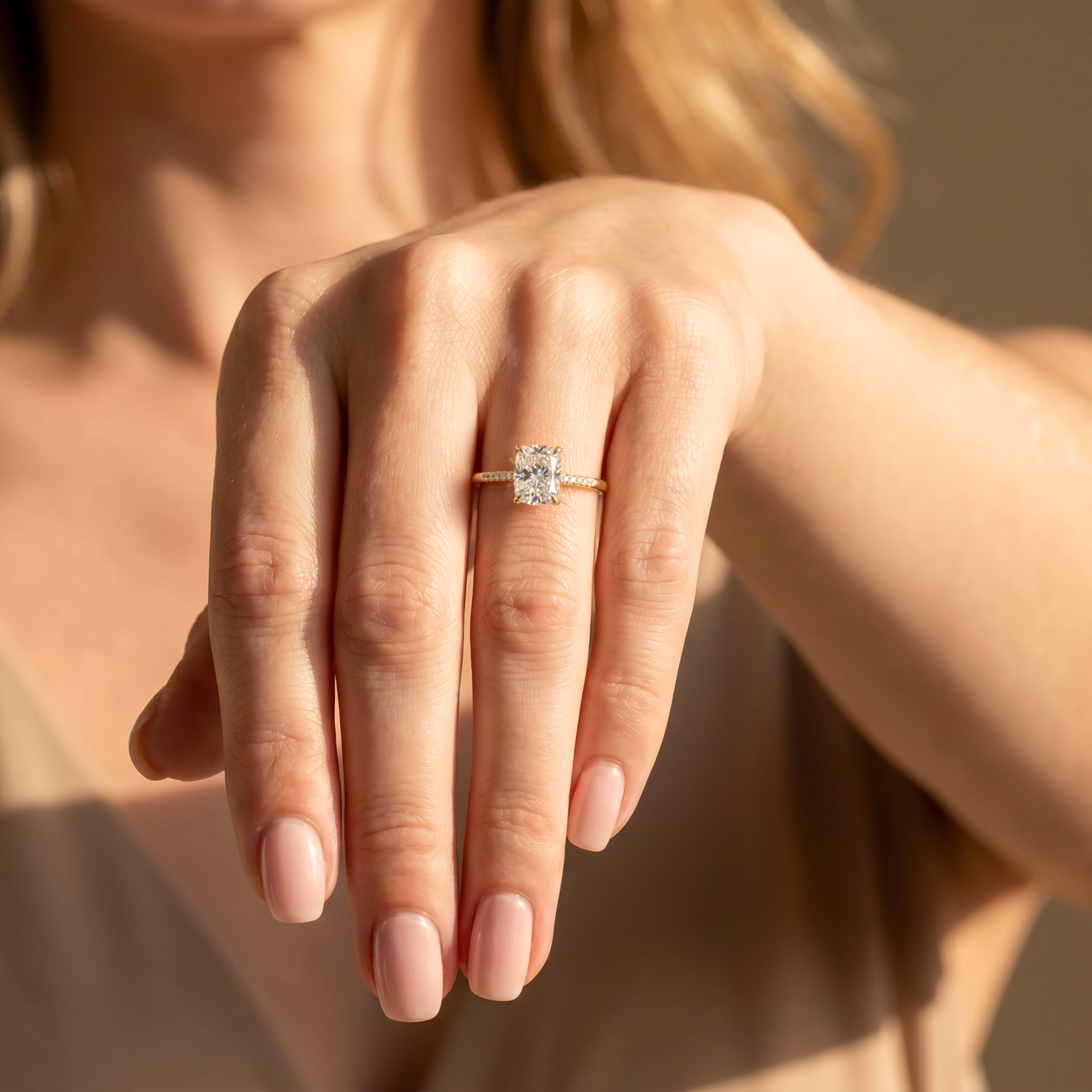 A woman's hand showcasing a cushion cut moissanite engagement ring set in a yellow gold band.