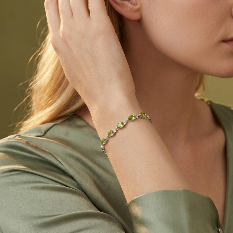 Sterling silver bracelet with pear-cut green peridot gemstones worn on a woman's wrist with a green silk blouse.