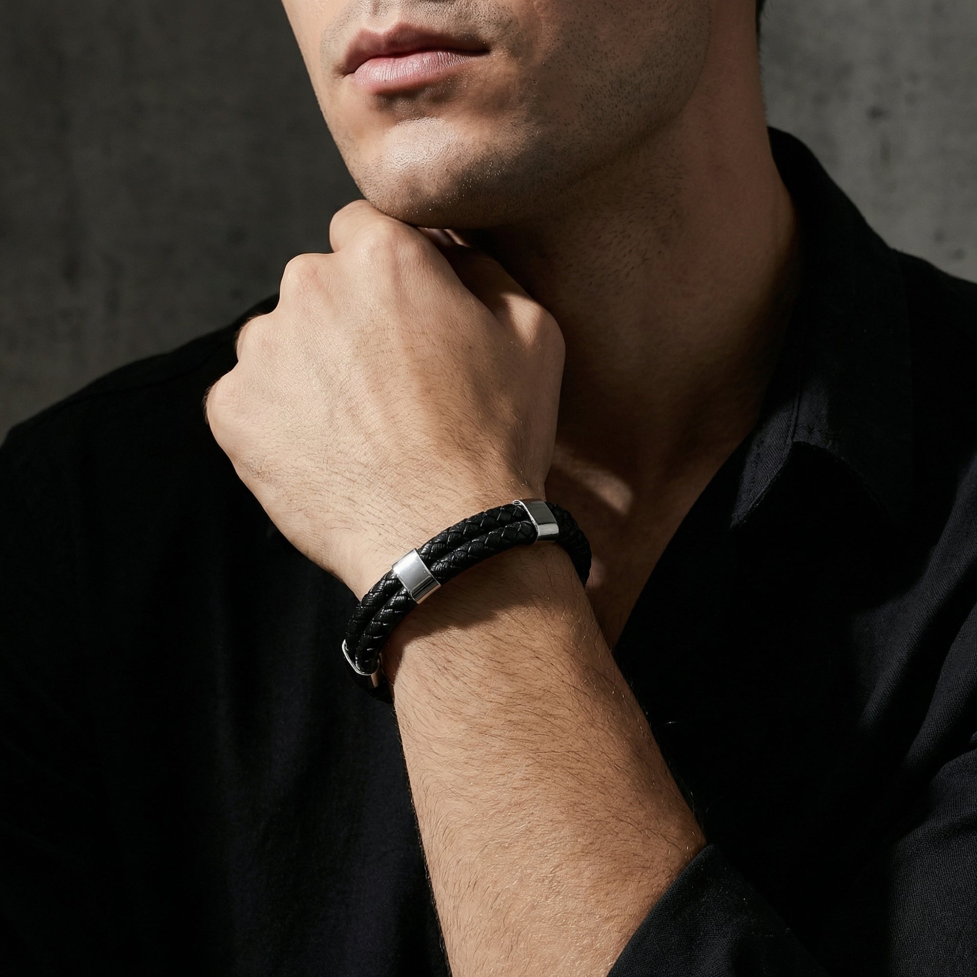 Men's black double-braided leather bracelet with silver stainless steel accents worn on a model's wrist.