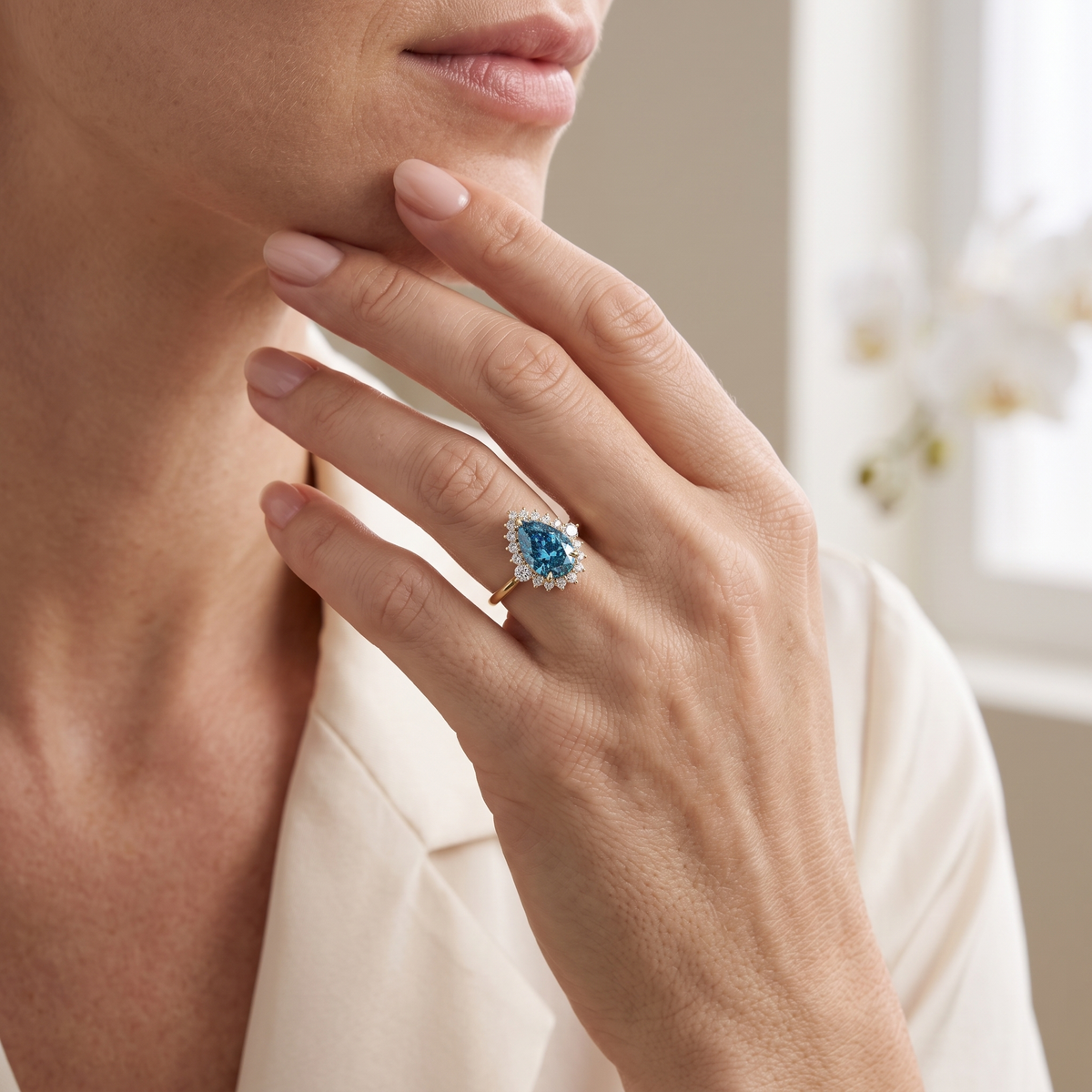 Model wearing a pear-cut blue moissanite halo ring in rose gold touching her chin.