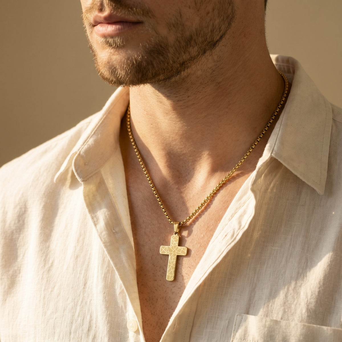 Gold-toned geometric cross necklace worn around a man's neck over an open white linen shirt.