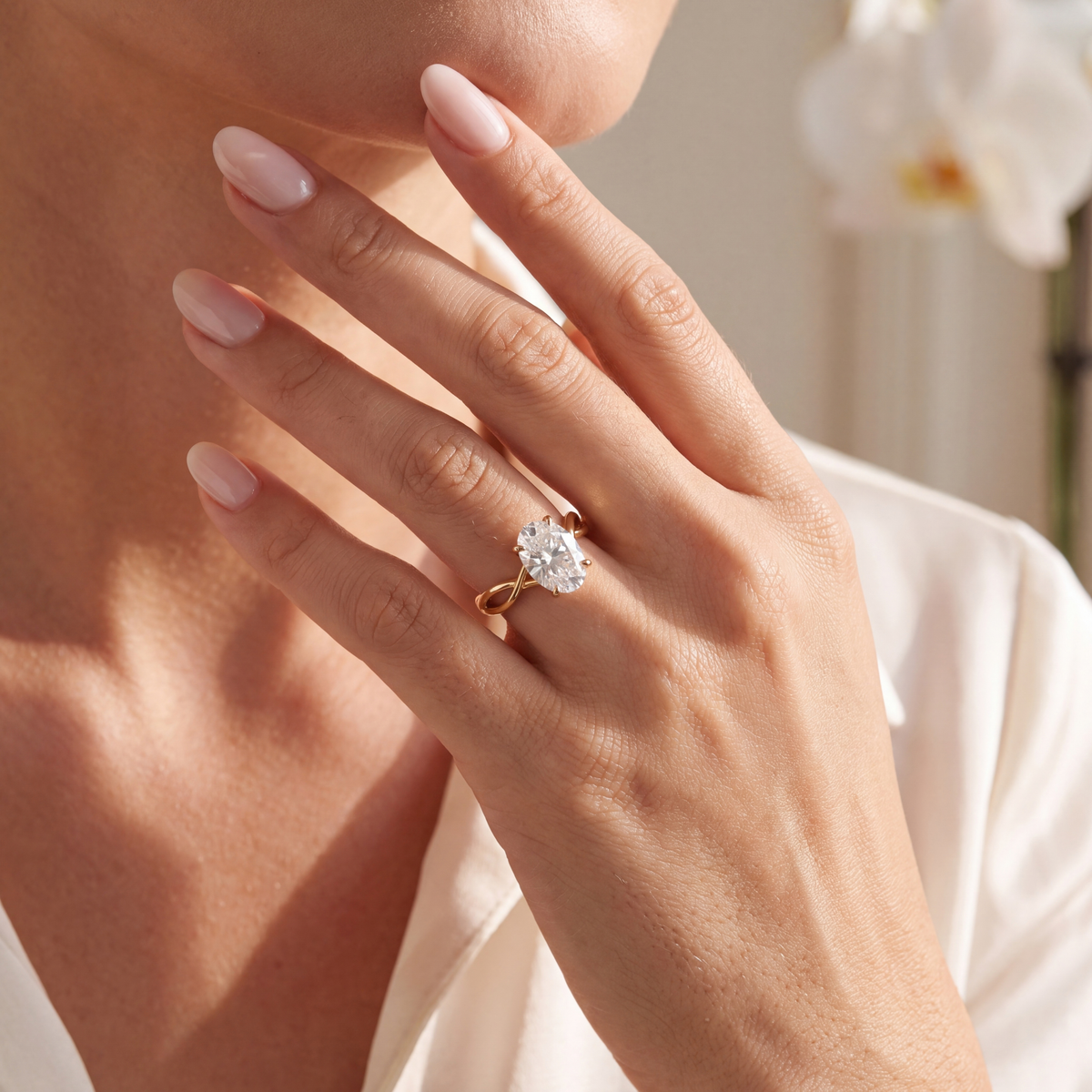 Close-up of a model wearing an oval moissanite engagement ring in yellow gold.