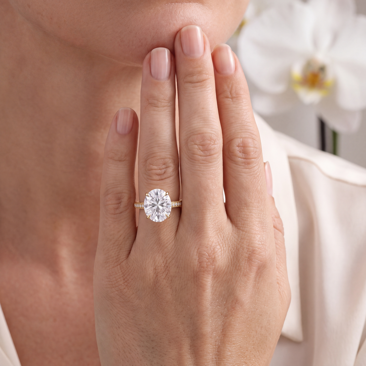 Yellow gold oval moissanite engagement ring with a milgrain pave band shown on a hand.