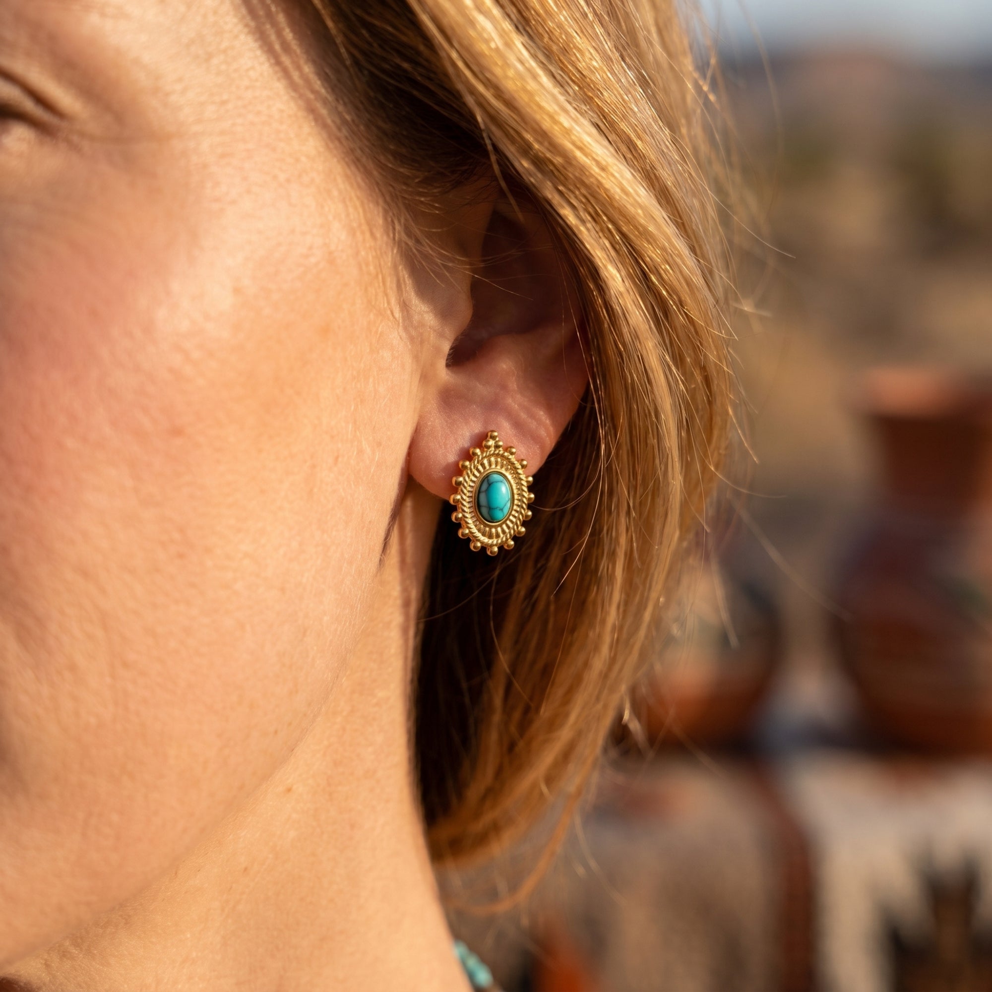 Woman wearing a gold-tone Southwestern drop earring with an oval turquoise-hued stone.