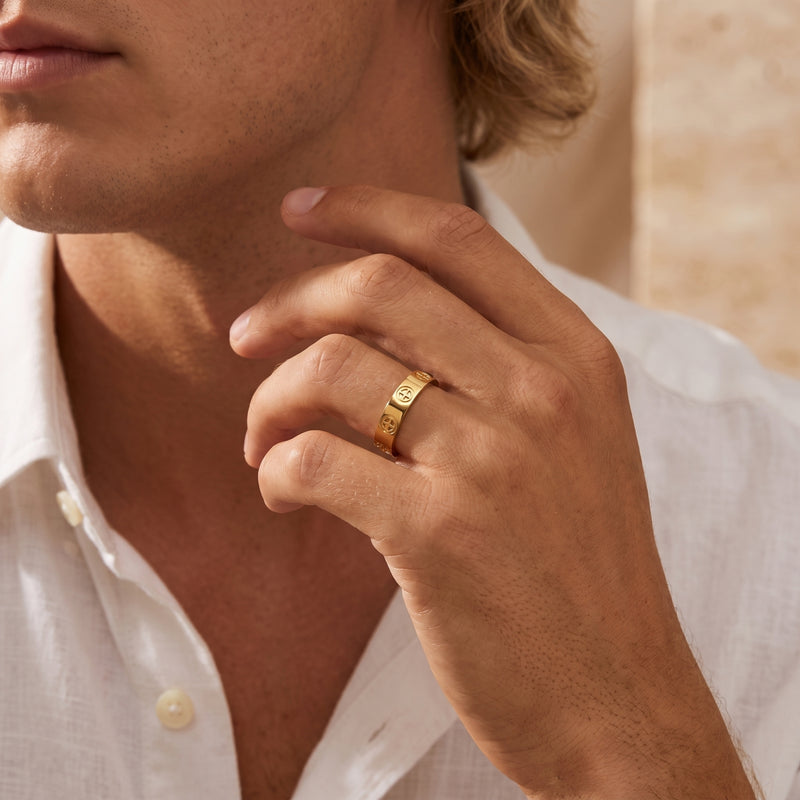 Man wearing a gold-tone cross band ring with circular cross motifs, dressed in a white linen shirt.