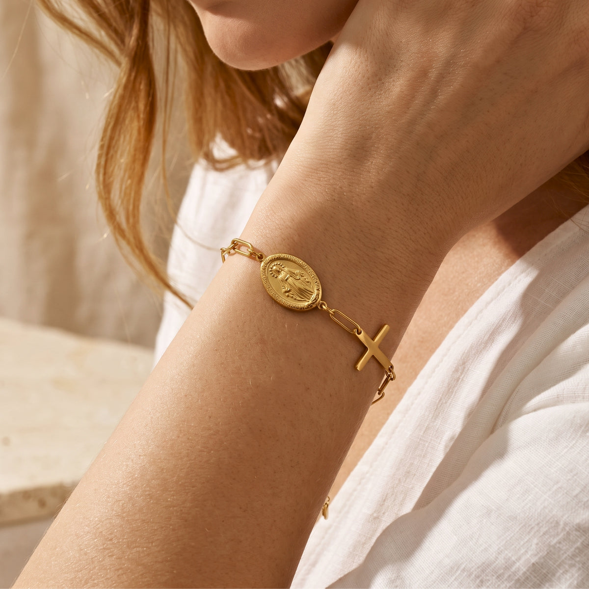 Gold-tone link bracelet with an oval religious medal and cross charm shown worn on a wrist.