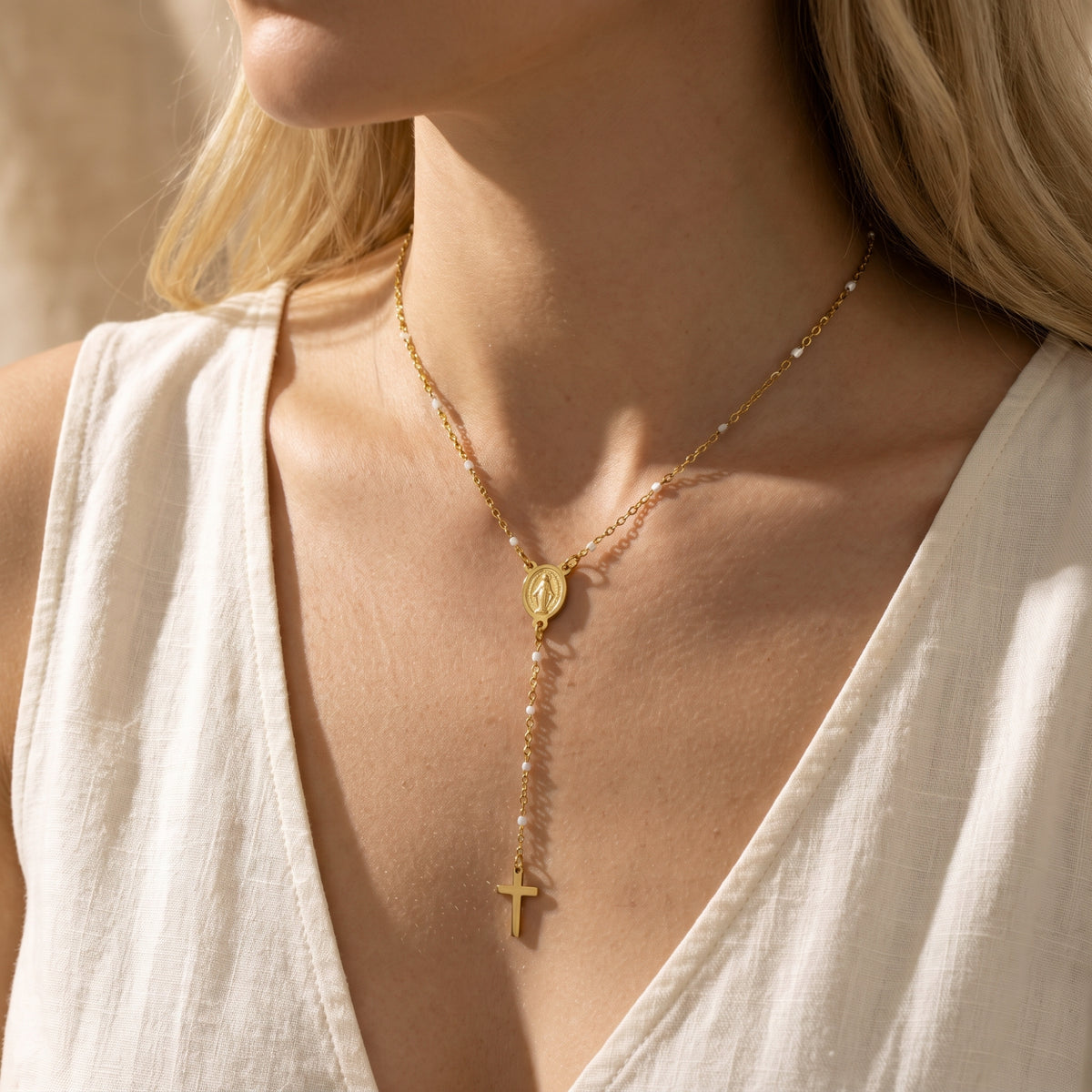 Close-up of a model wearing a gold-tone rosary lariat necklace with a cross drop over a white top.