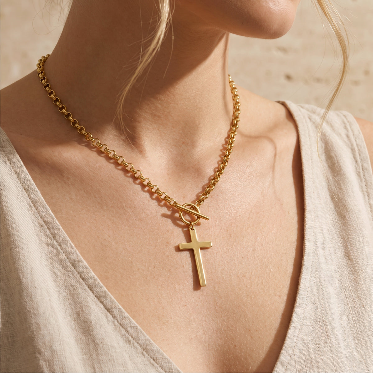 Model wearing the gold-tone toggle cross necklace with a light neutral V-neck top.