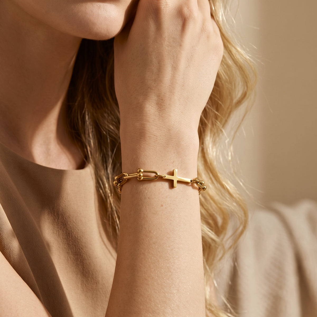 Close-up of a gold-tone U-link cross bracelet worn on a wrist against a neutral beige top.