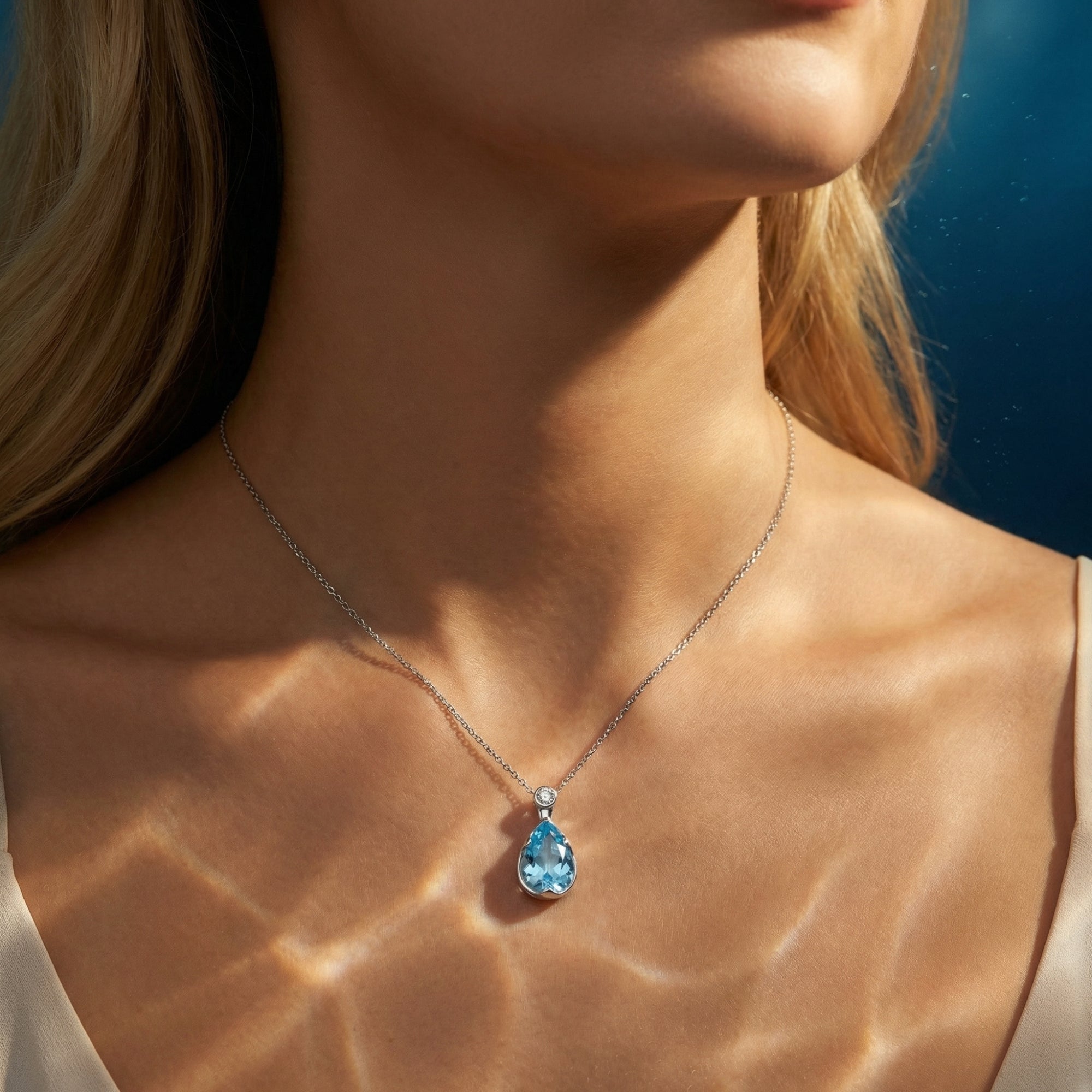 Woman wearing the pear cut aquamarine pendant necklace in platinum, featuring a dappled light effect on her neck.