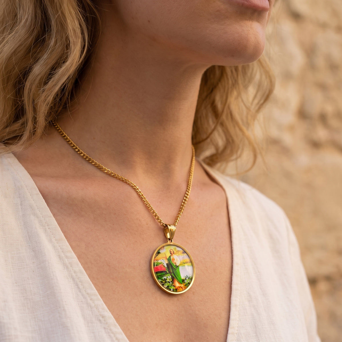 Woman wearing the round gold-tone St. Jude medallion necklace over a white top.