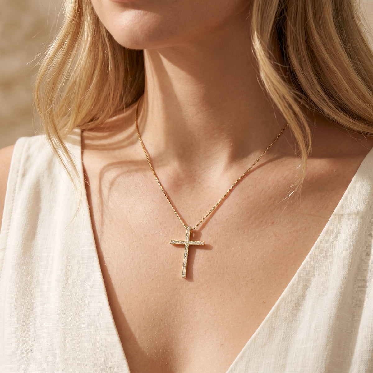 Gold-tone pavé cross necklace worn at the neckline of a cream V-neck top.