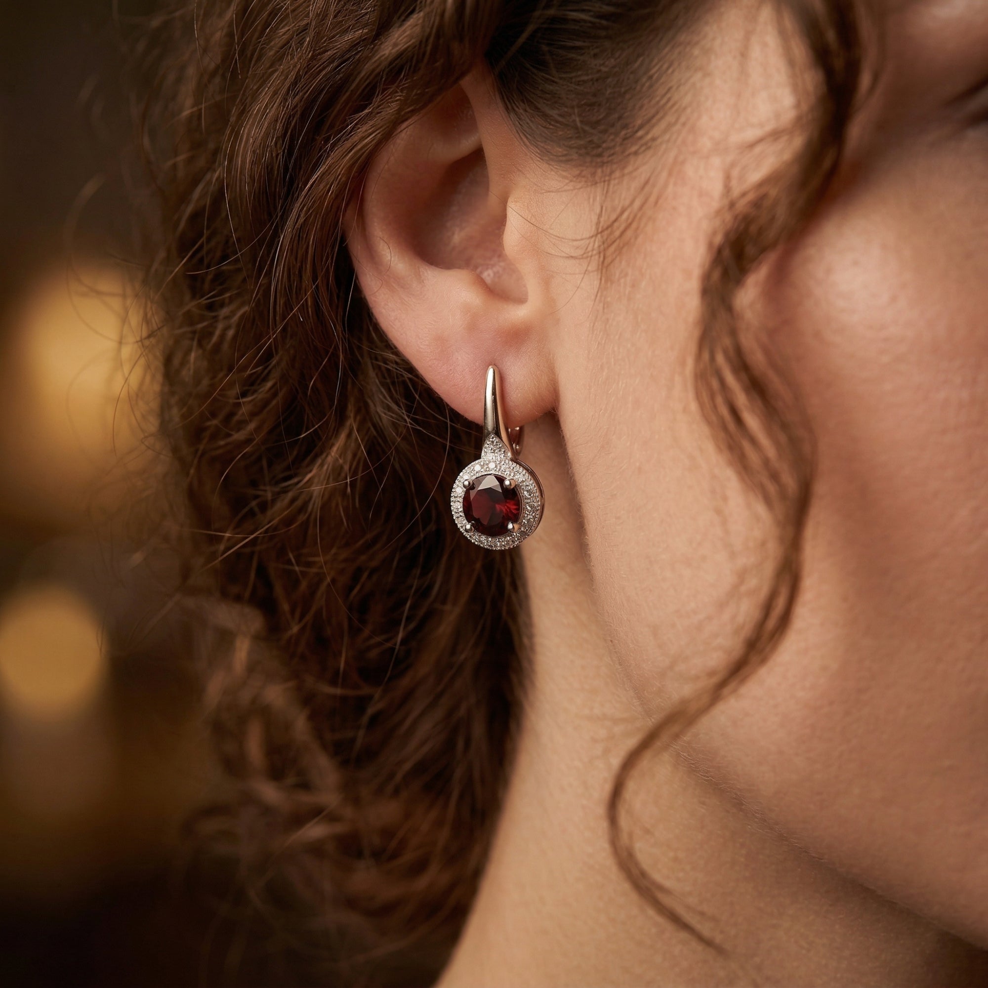 Model wearing a Novella drop earring featuring a round burgundy garnet and silver halo setting.