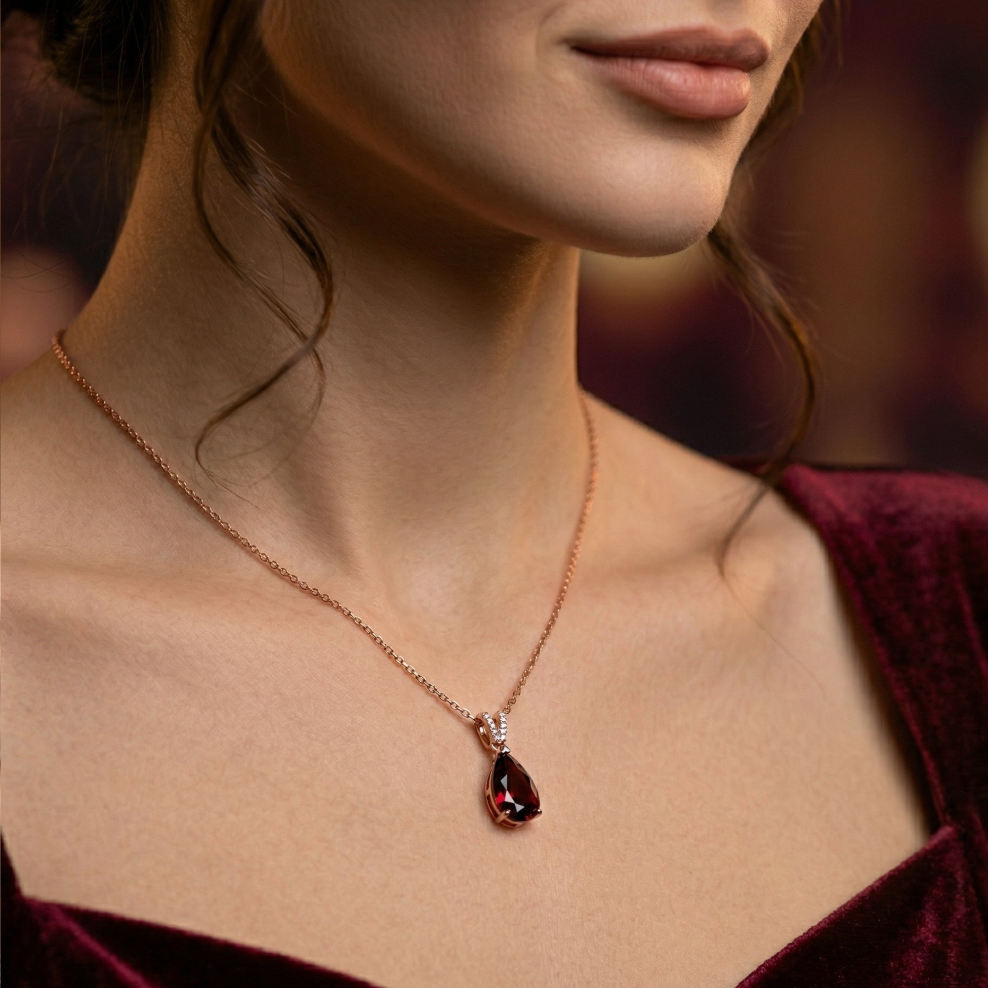Model wearing the Ignia pear cut garnet necklace in 18K rose gold with a burgundy velvet dress.