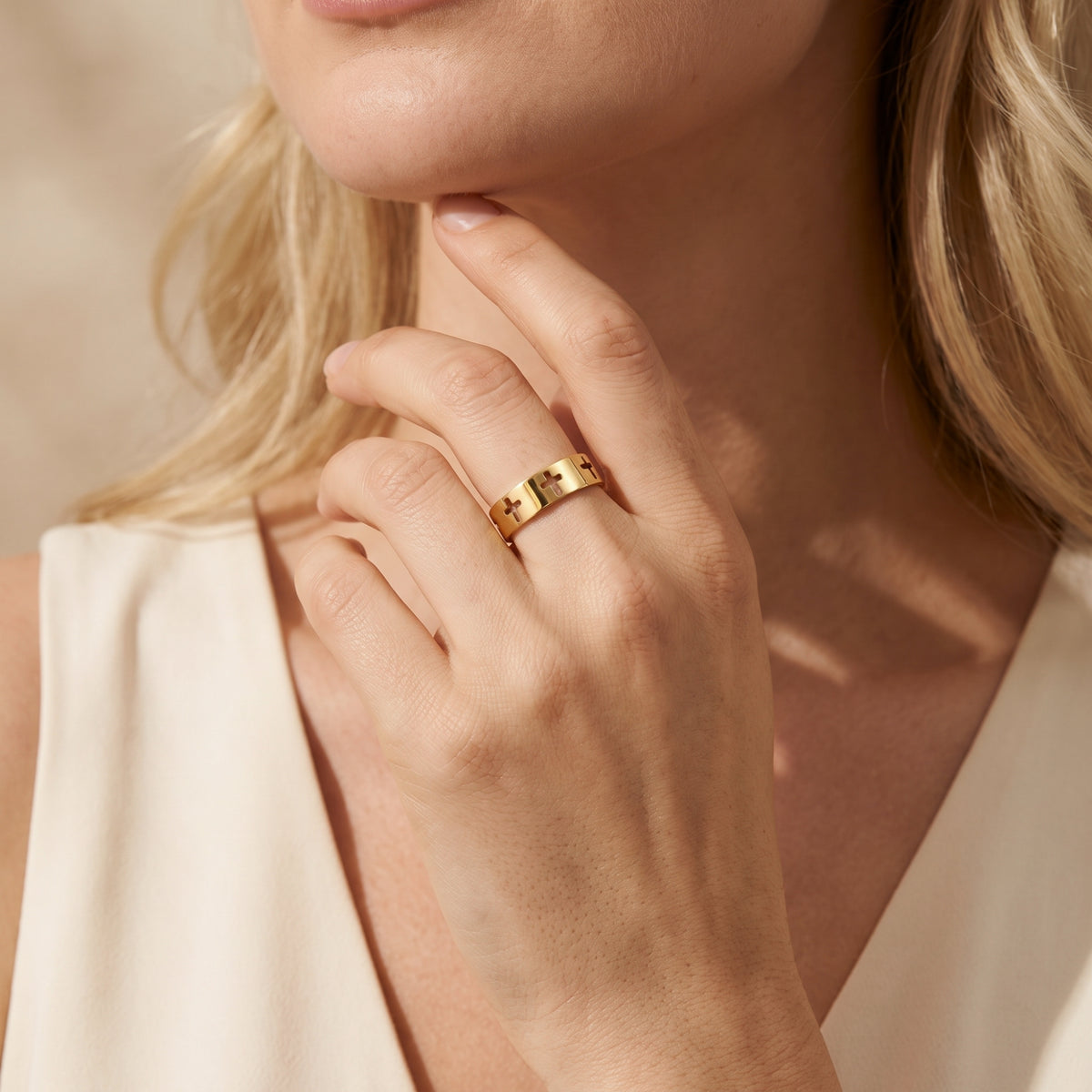 Model wearing the gold-tone cutout cross band ring with her hand raised near her chin.