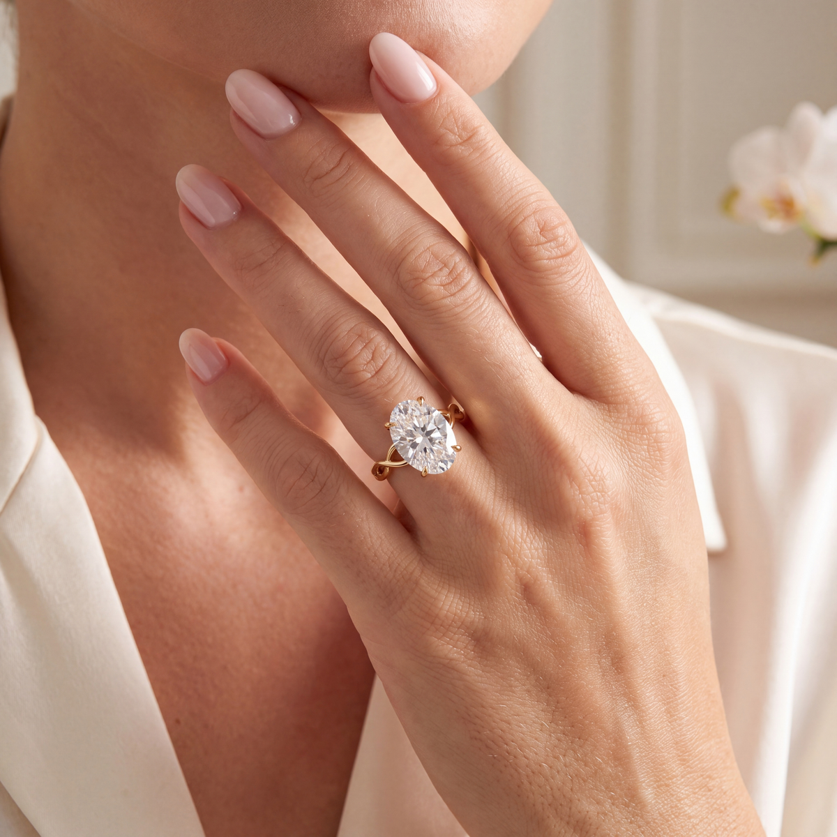 An oval moissanite yellow gold ring with a twisted band worn on a model's hand.