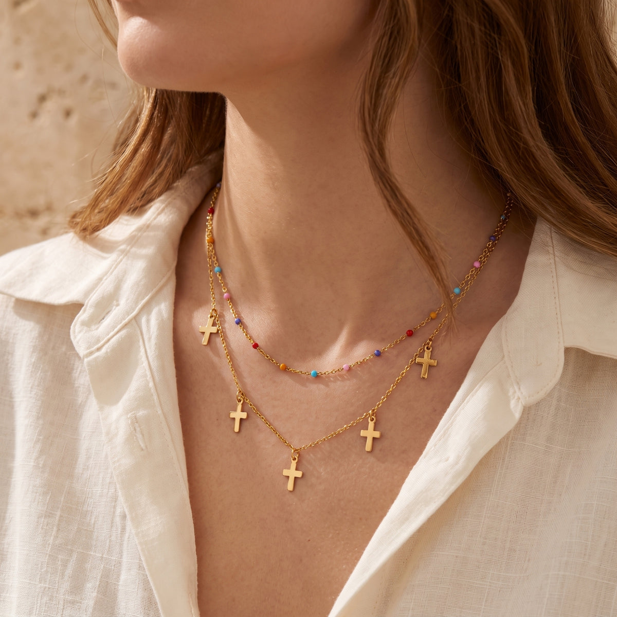 Side-angle view of a model wearing the layered gold-tone cross necklace with colorful beads over a white shirt.