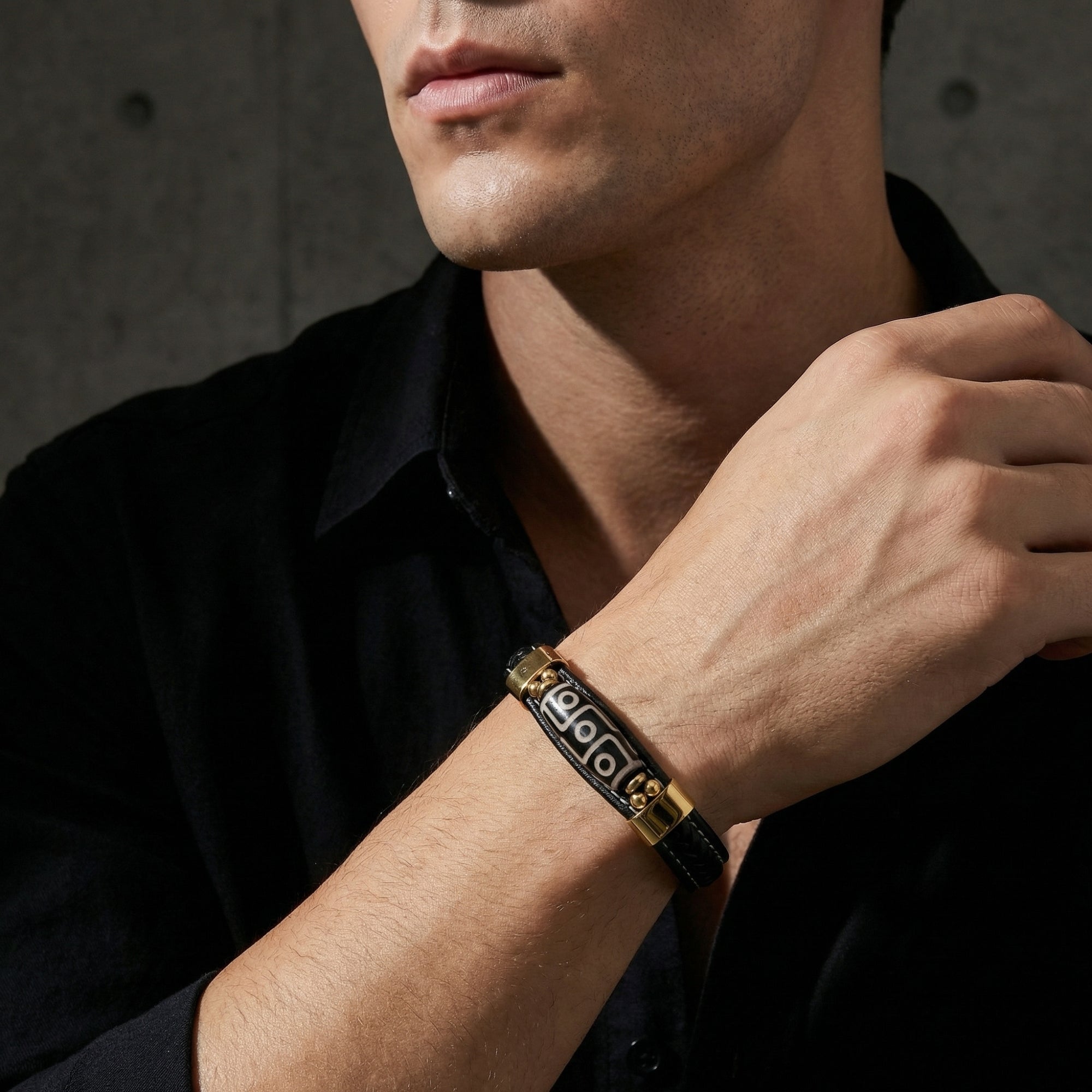 The Enigma gold and black leather bracelet worn on a man's wrist against a dark background.