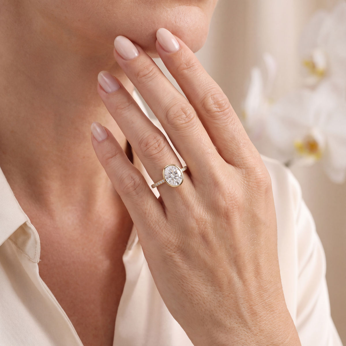 Yellow gold oval moissanite bezel engagement ring worn on a hand touching the chin.