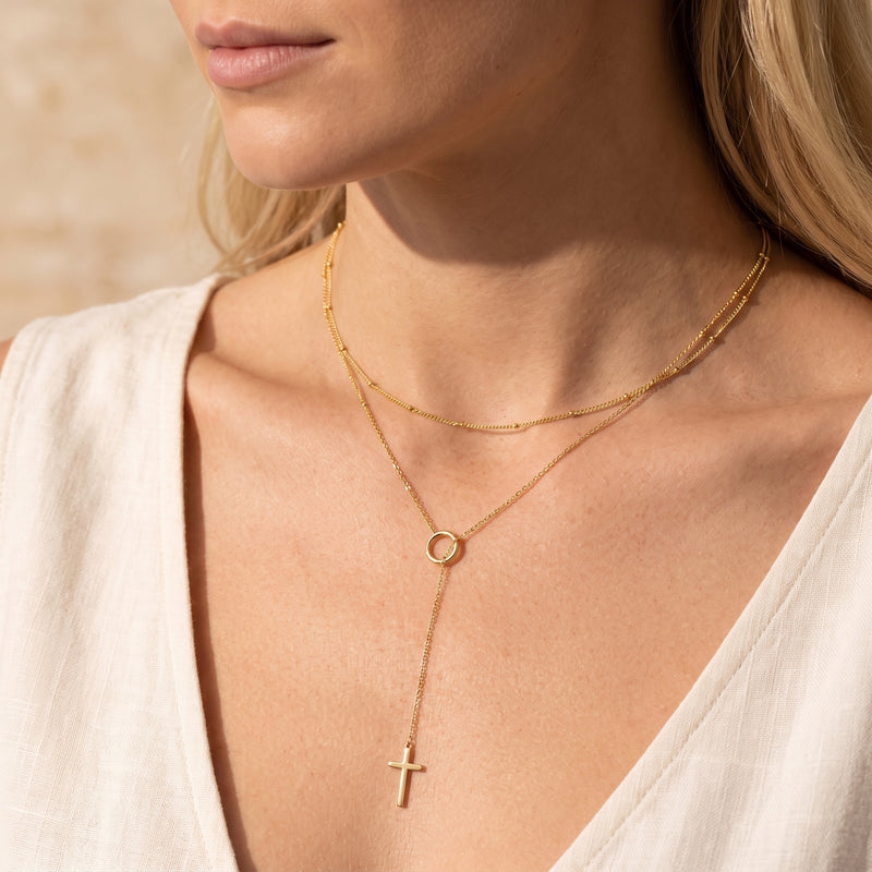 Close-up of a model wearing the gold-tone layered lariat necklace with a ring station and cross drop pendant.