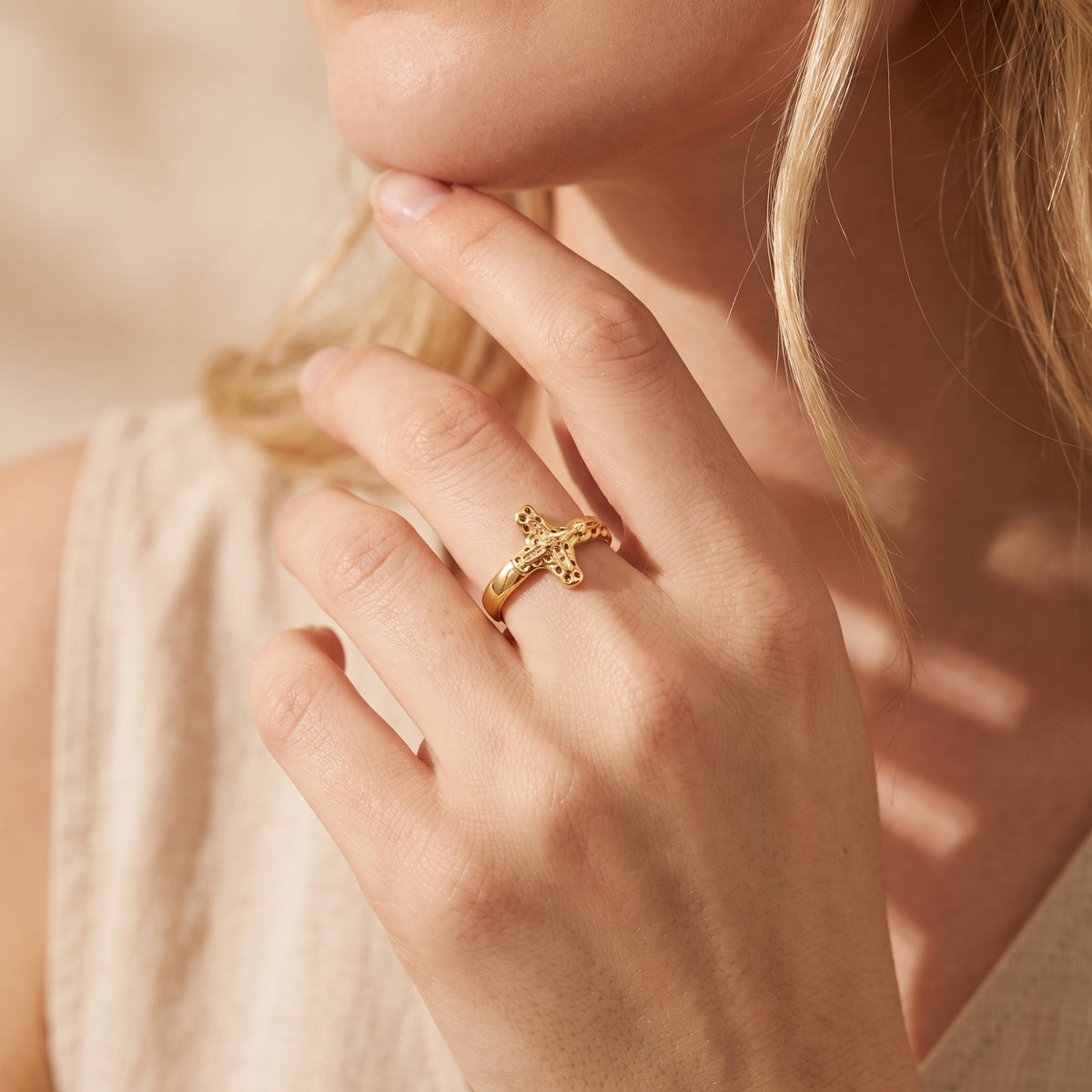Gold-tone sculpted cross ring worn on a woman's finger in a close-up near her face.